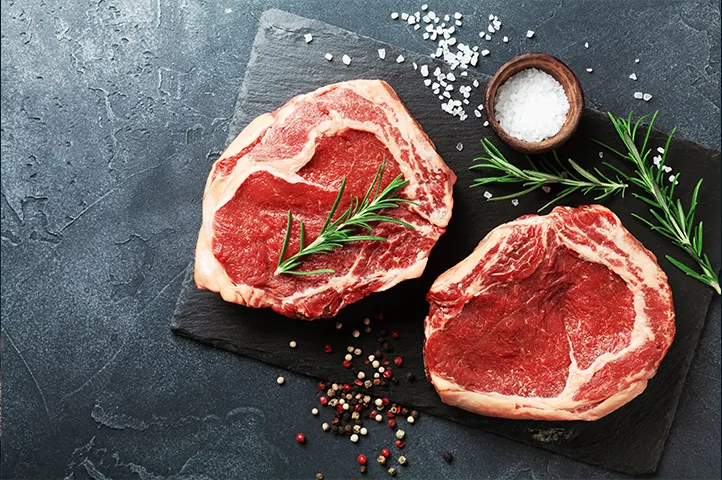 two slabs of meat on a slate surrounded by salts and rosemary sprigs